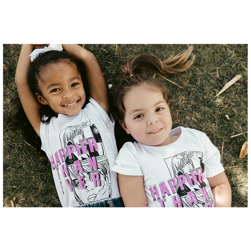 Two children lying on grass, wearing white "Didn't Change My Number" organic youth T-shirts from Billie Eilish merch, and smiling.