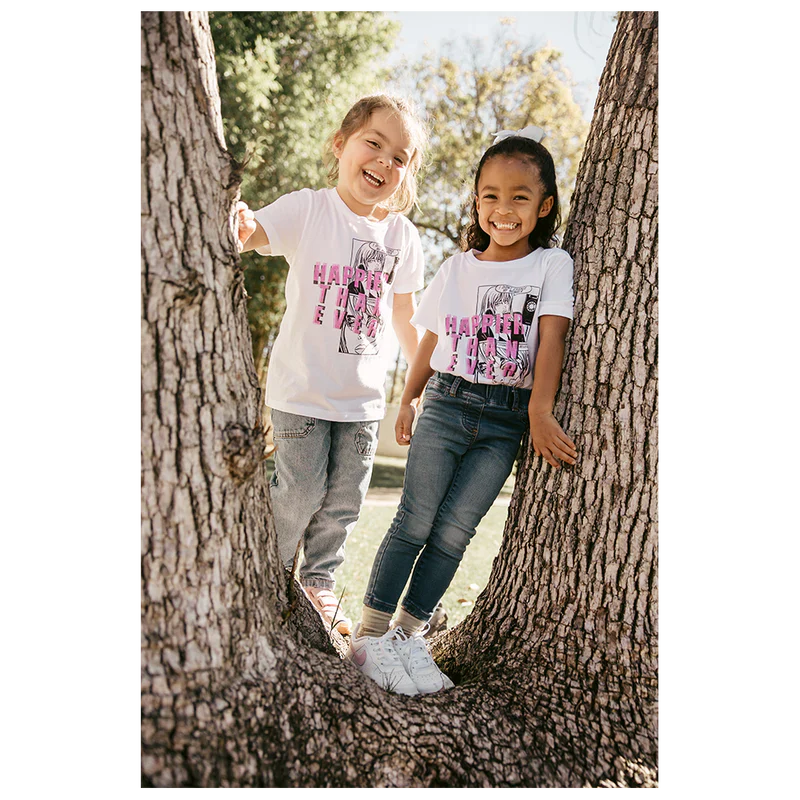 Two children climbing trees, wearing white "Didn't Change My Number" organic youth T-shirts from Billie Eilish merch, and smiling.