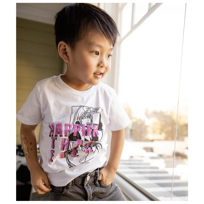 Child looking out of a window, wearing a white "Didn't Change My Number" organic youth T-shirt from Billie Eilish merch.