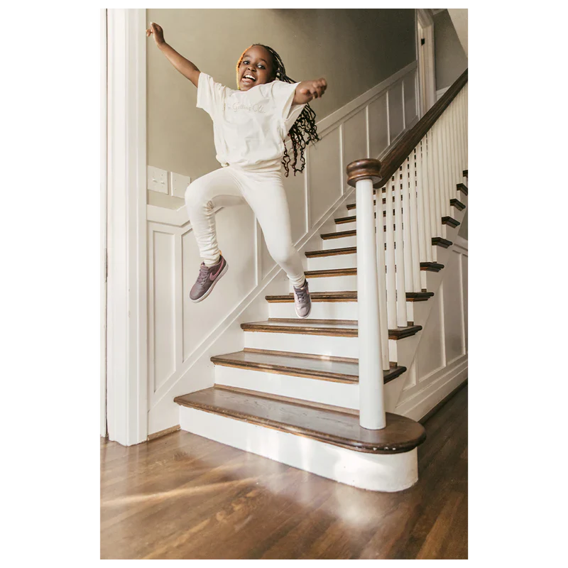 Child jumping on stairs wearing a white "I'm Getting Older" organic youth T-shirt from Billie Eilish merch, smiling and mid-air