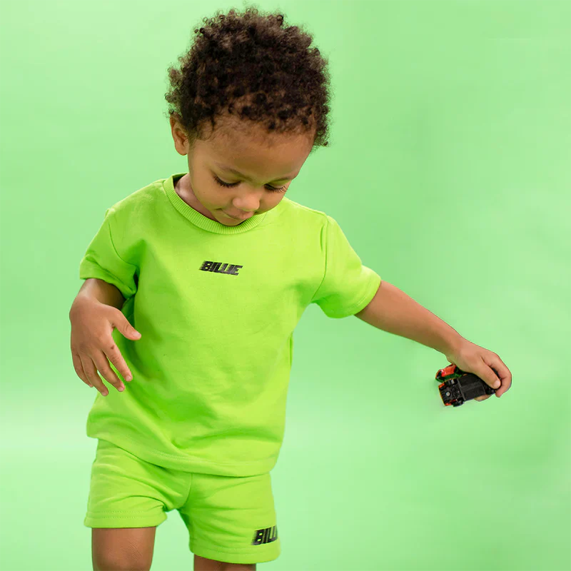 Child wearing a bright green Billie T-Shirt and shorts set with "BILLIE" text, part of the Billie Eilish merch collection.