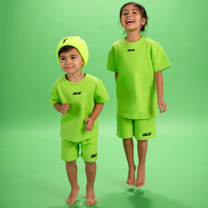 Two children in bright green Billie T-Shirts and shorts from Billie Eilish merch, jumping and smiling.