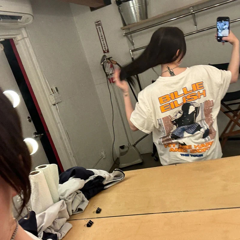 Billie Eilish taking a mirror selfie wearing the Hit Me Hard And Soft Tour Tee showing the tour design on the back