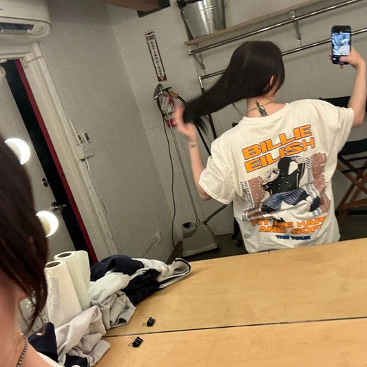 Billie Eilish taking a mirror selfie wearing the Hit Me Hard And Soft Tour Tee showing the tour design on the back