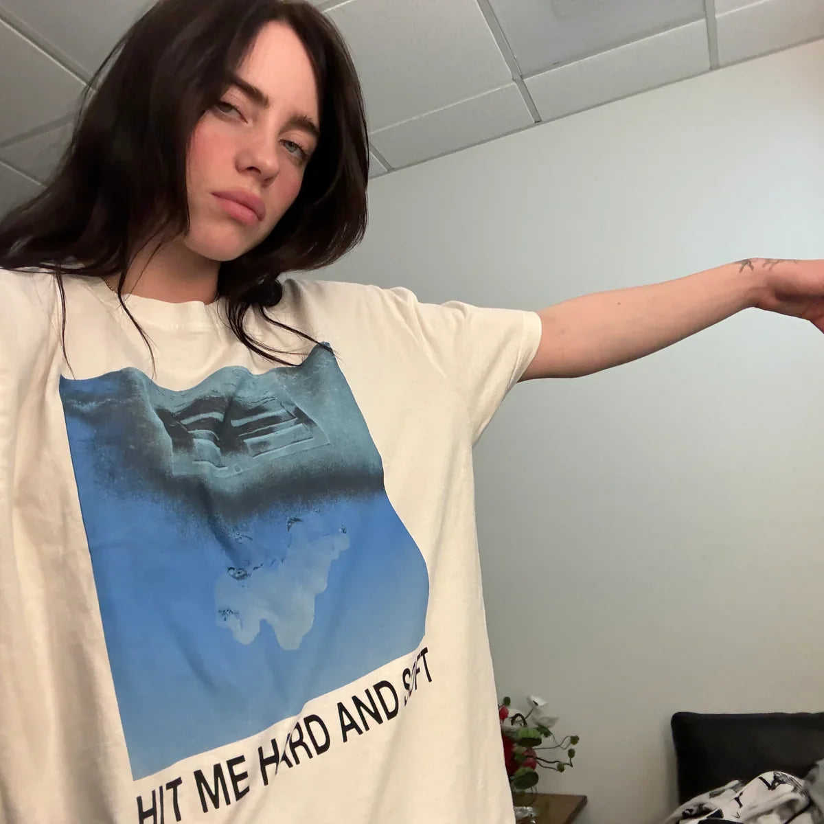 Billie Eilish wearing the Hit Me Hard And Soft White Cover Tee featuring a blue graphic design on a white t-shirt.