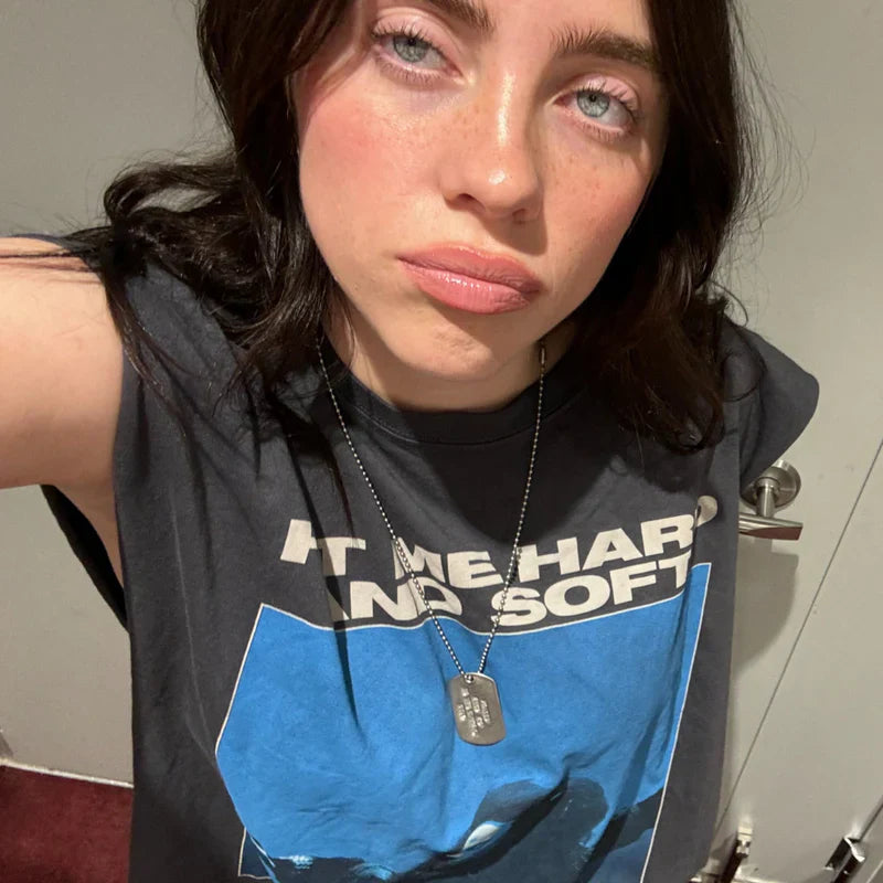 Billie Eilish wearing the Tracklist Cutoff Muscle T-Shirt featuring a graphic design with 'HIT ME HARD AND SOFT' text in blue